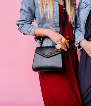 Fashion details of two pretty women posing together over pink isolate background.  Autumn trendy outfit.Similar  jeans jacket. Stylish sunglasses. Leather bag.